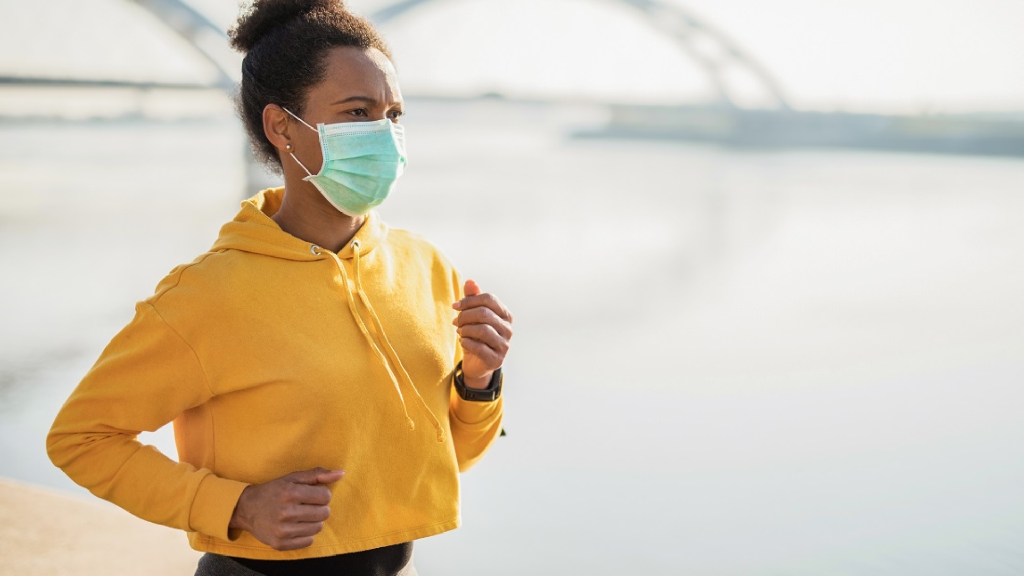 Mid adult African American woman running in the city next to the river and wearing a protective face mask. Corona Virus Outbreak.